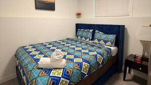 Um quarto com cama, mesa de cabeceira, luminária, janela com persianas e luz no teto.
