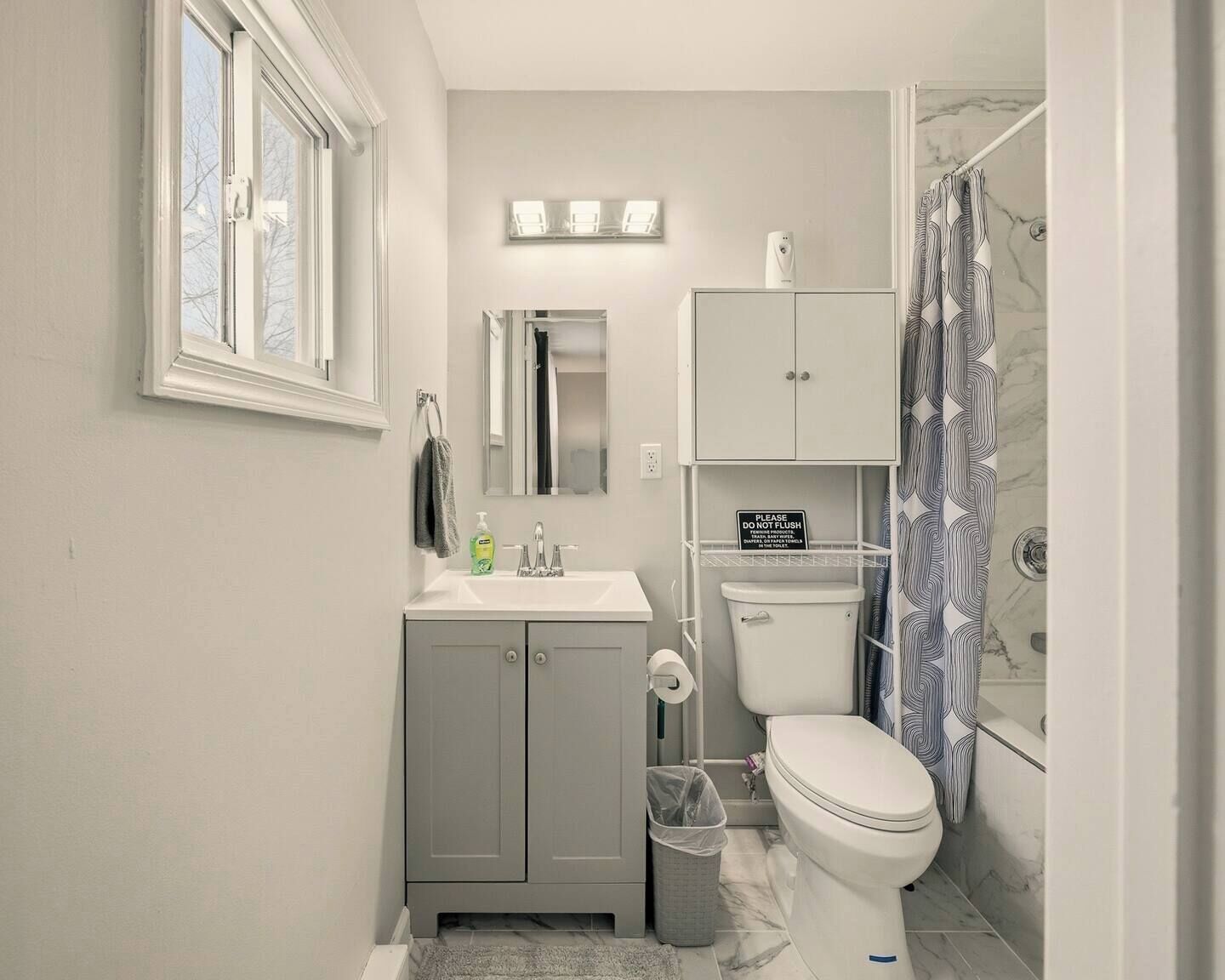 A compact bathroom with a toilet, sink, and cabinet, a window, and a shower curtain.