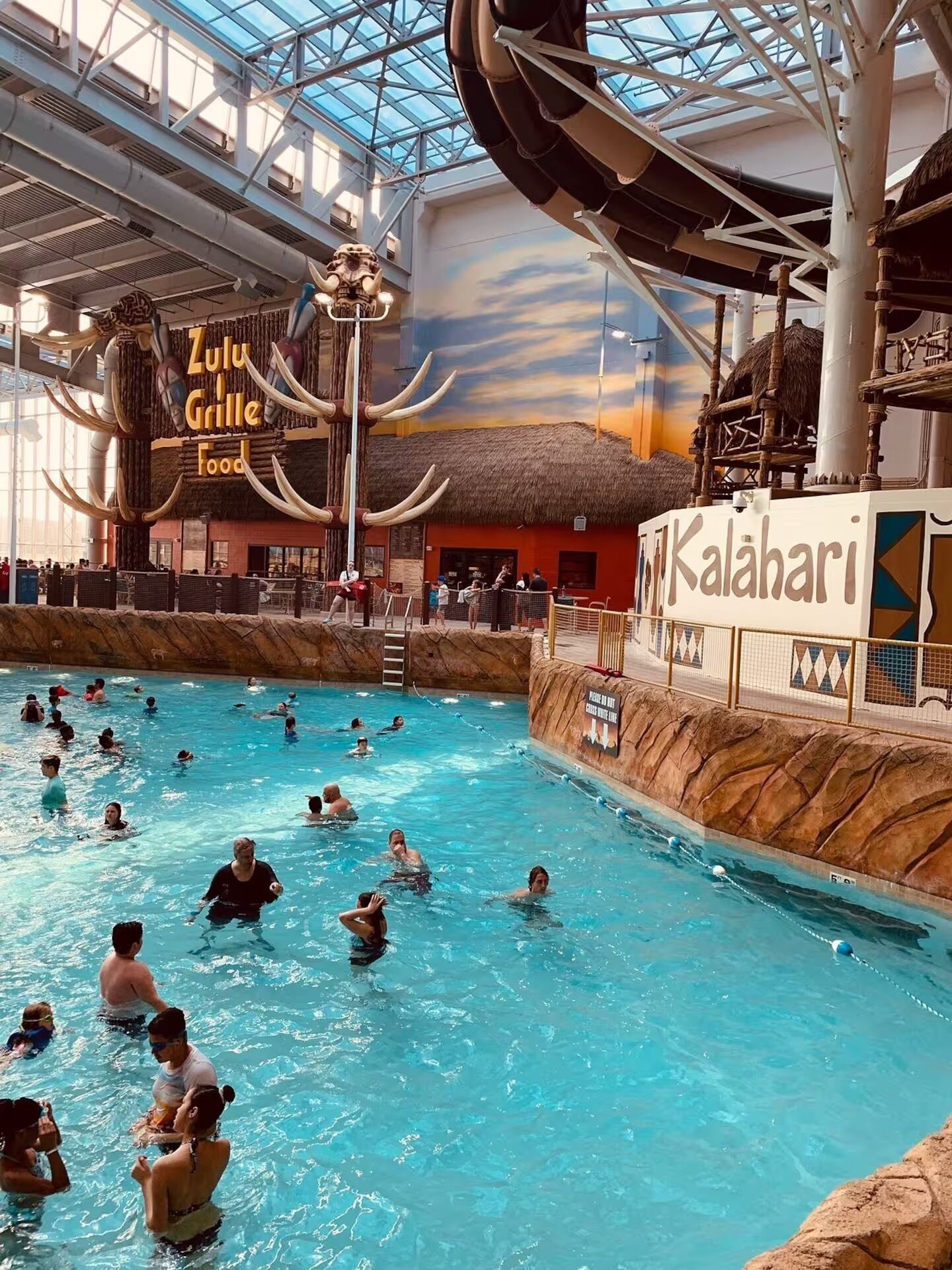 An indoor swimming pool with a thatched-roof structure labeled 'Zulu Grille Food' and a sign for 'Kalahari.'
