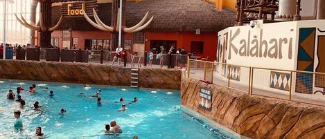 An indoor swimming pool with a thatched-roof structure labeled 'Zulu Grille Food' and a sign for 'Kalahari.'