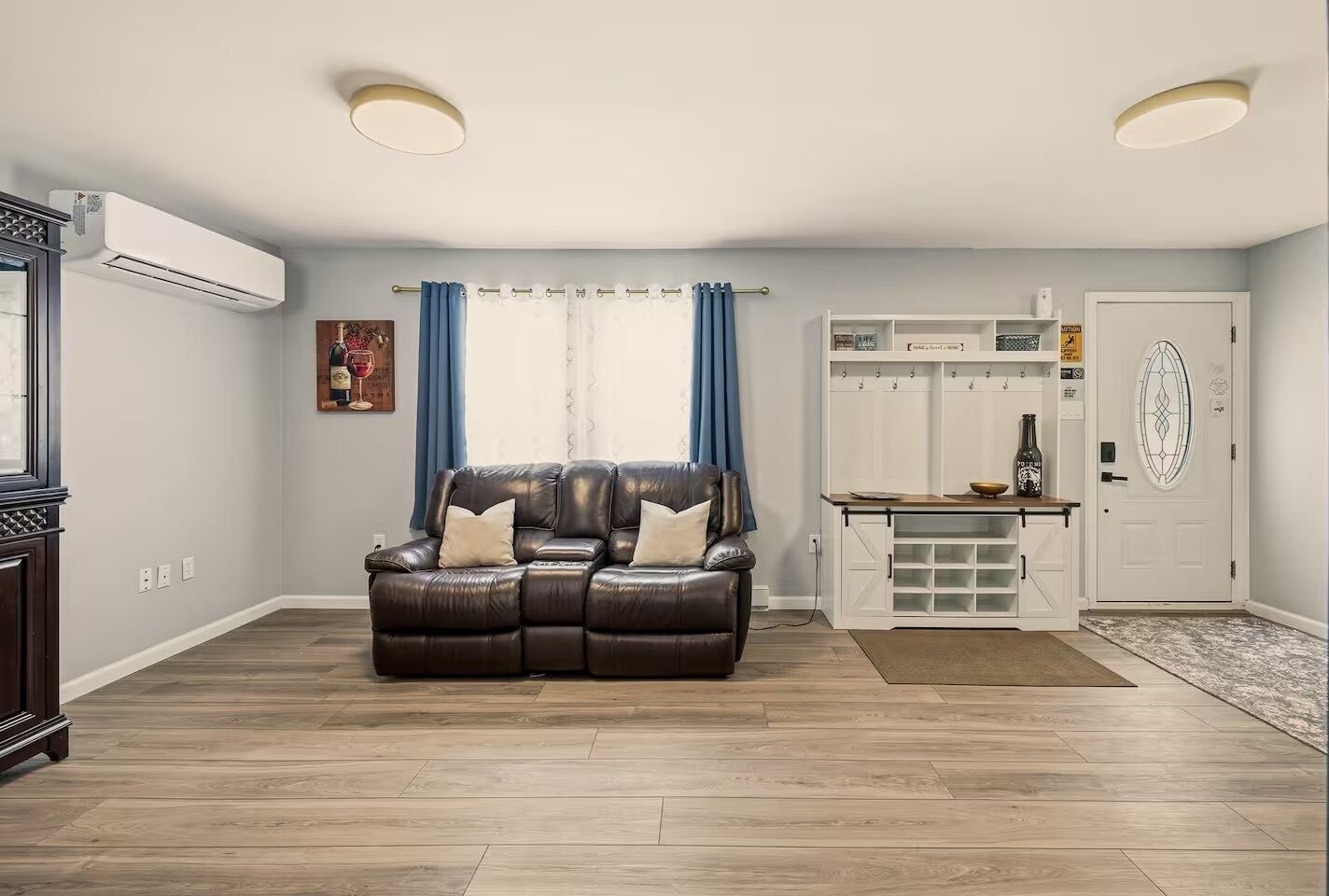 Un salon avec un canapé en cuir, un meuble blanc et une porte ornée d’un panneau de verre décoratif.