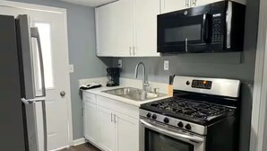A kitchen with white cabinets, a black microwave, a stainless steel stove, and a refrigerator. - Entire Unit D - Bold & Exclusive-1BR (Forsyth)