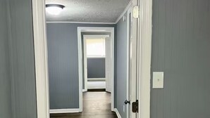 A hallway with wooden flooring and light blue walls, leading to a room with a window. - Entire Unit D - Bold & Exclusive-1BR (Forsyth)