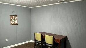 A dining area with a table and two chairs, a textured ceiling, and a wall-mounted decoration. - Entire Unit D - Bold & Exclusive-1BR (Forsyth)