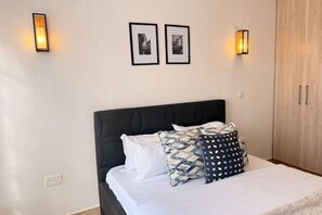 Un dormitorio con cama, dos cuadros en la pared y dos luces fijadas a la pared.