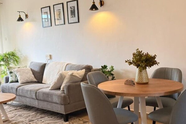Una sala de estar con un sofá, sillas, una mesa redonda de madera y una planta en maceta.