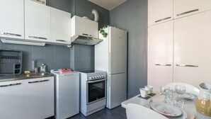 Eine kompakte Küche mit weißen Schränken, einem Einbauofen, einem Kühlschrank und einem Essbereich mit Tisch für zwei Personen.