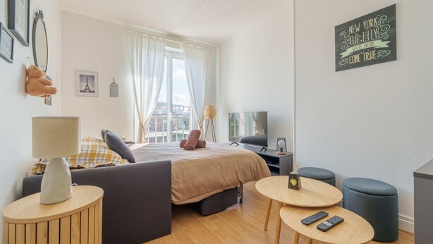 Ein modernes Hotelzimmer mit Bett, Schreibtisch, Stuhl, rundem Tisch und Fernseher.