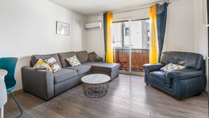 Una sala de estar con un sofá seccional, una mesa de centro redonda, un sillón azul y vistas a través de un ventanal.