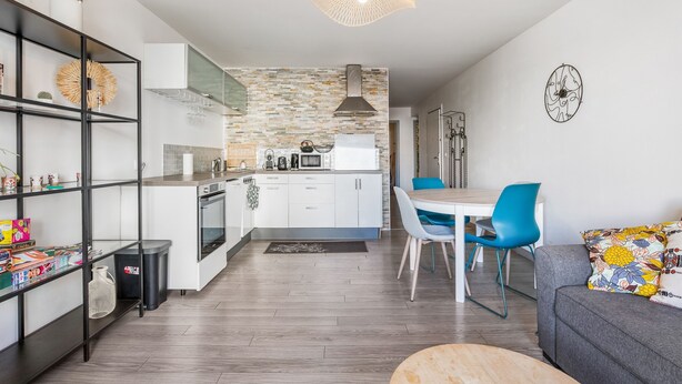 Una cocina moderna con armarios blancos, un salpicadero de piedra y un comedor con una silla azul y una mesa blanca.