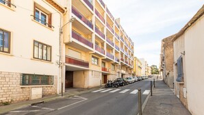 Un edificio residencial de varios pisos con balcones, coches estacionados y una calle despejada.
