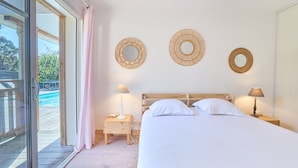 Un dormitorio con cama, dos mesitas de noche, ventana con vistas y tres espejos redondos en la pared.