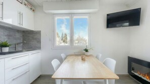 Eine moderne Küche mit weißen Schränken, einem Holzespeisetisch, weißen Stühlen, einem Fernseher und einem Kamin.