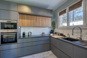 A modern kitchen with a built-in oven, a sink, and wooden cabinets. - Les Dunes Blanches - A quelques pas de la plage (Saint-Georges-de-Didonne)