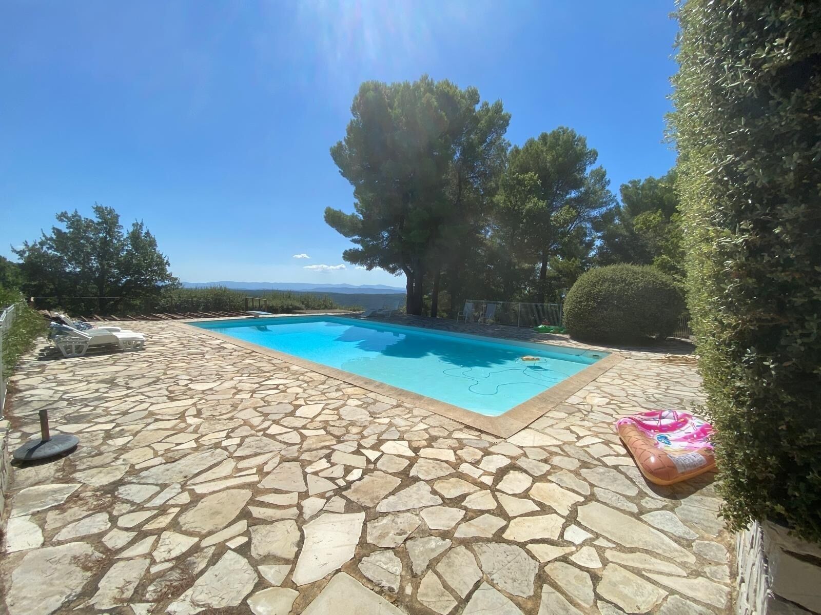 A swimming pool with stone tiles, lounge chairs, and a view of the landscape.