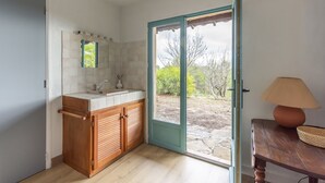 A bathroom with a wooden vanity, a mirror, and a door leading to a garden. - Hameau des Laurons - Climatisée, piscine privée (Tourtour)