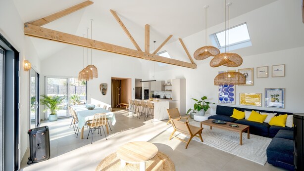 A spacious living area with a high ceiling, wooden beams, a dining area, and a kitchen.
