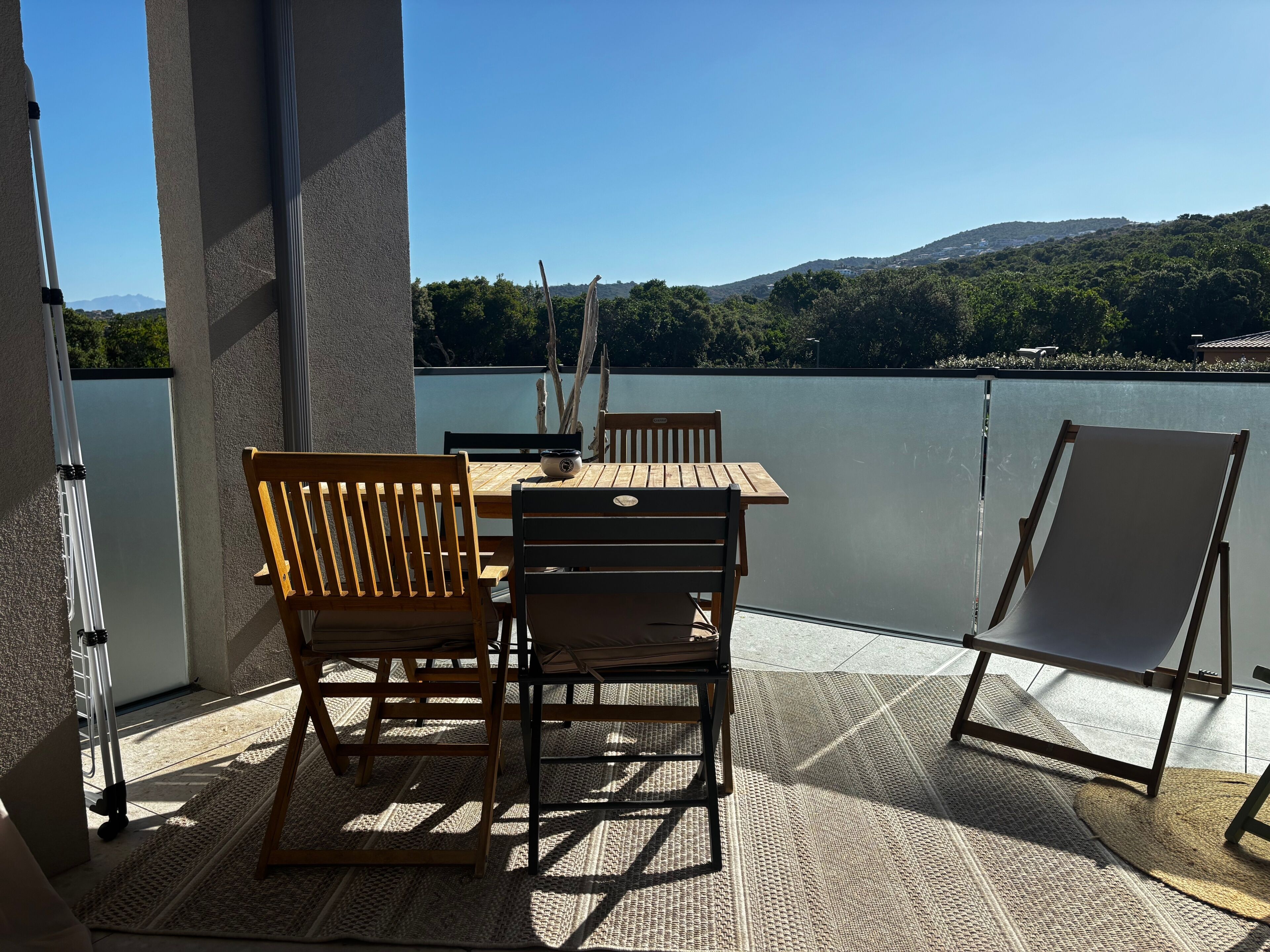 A terrace with a table and chairs, a view of a lake, and a chair for sunbathing.