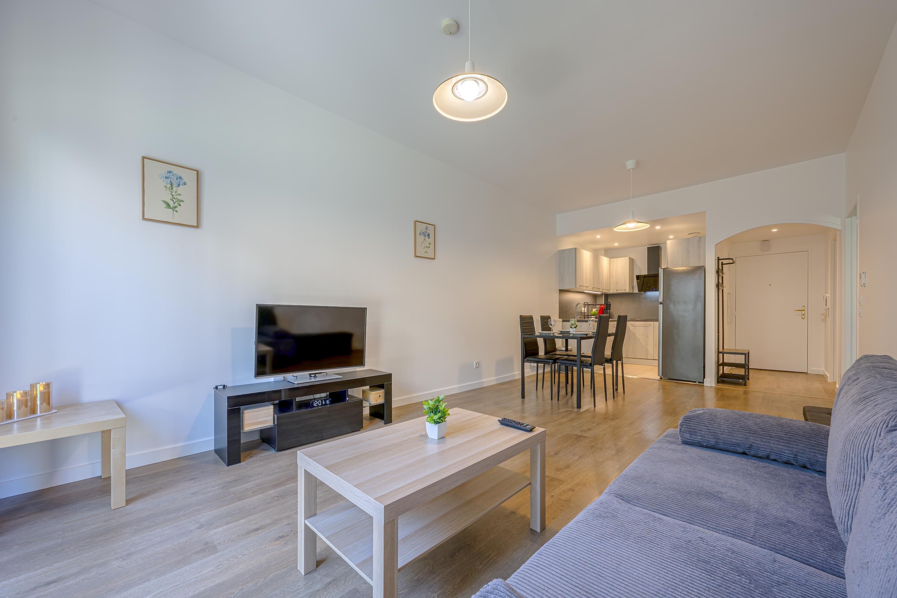 Een moderne woonkamer met een flatscreen televisie, een salontafel, een bank en een eethoek met stoelen en een tafel.