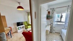 A living area with a TV, green chair, red sofa, and a small table with a fan. - Poppy of SteraM Flats Torremolinos (Torremolinos)