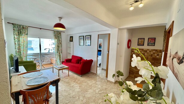 A living room with a red sofa, a dining area with a table and chairs, a balcony with a view, and a hallway leading to a bedroom. - Poppy of SteraM Flats Torremolinos (Torremolinos)