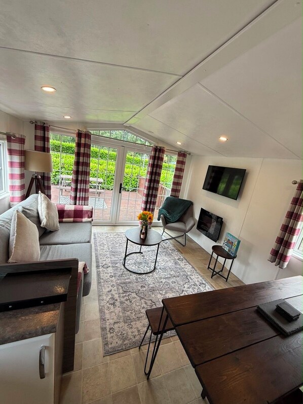 A modern living room with a sofa, a coffee table, a TV mounted on the wall, and a dining table. - Brae Lodge Dollar – A Relaxing Break (Dollar)