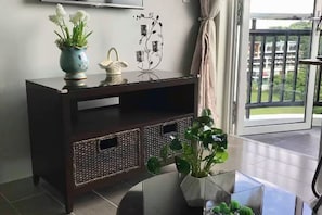 Une console en bois foncé, agrémentée d’objets décoratifs, un vase en verre contenant des plantes vertes et une vue sur un balcon avec une balustrade.