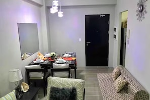 Un coin repas avec une table dressée pour quatre personnes, un canapé, une lampe et une porte noire.