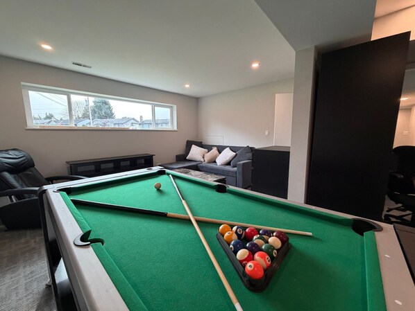 A pool table with balls, a sofa, and a window in a room. - Near Vancouver: Backyard Cinema + Game (Delta)