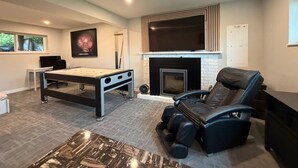 A modern living room with a pool table, a massage chair, a fireplace, and a mounted TV. - Near Vancouver: Backyard Cinema + Game (Delta)