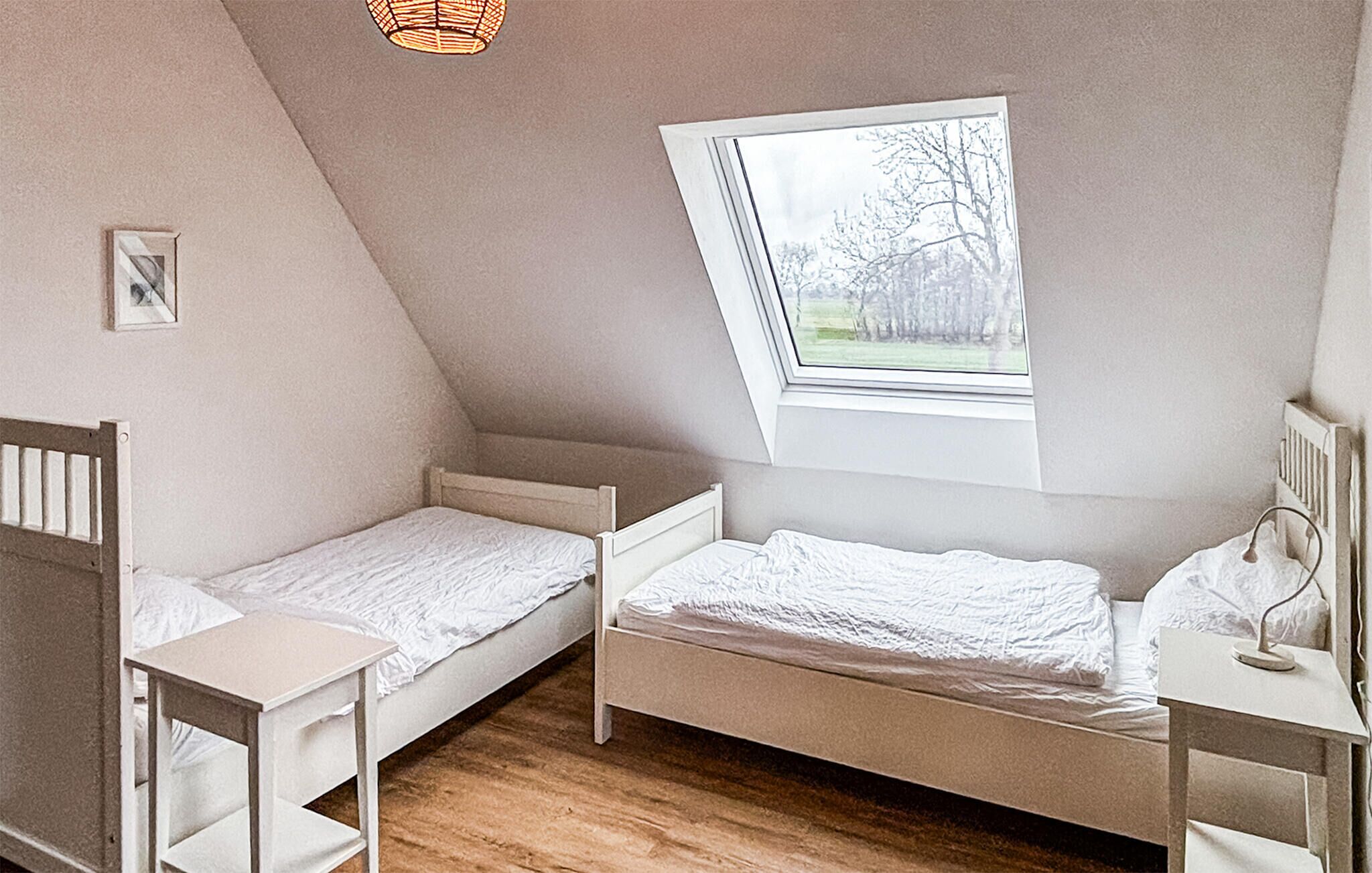 A small, single-room with two beds, a window, and a sloped ceiling.
