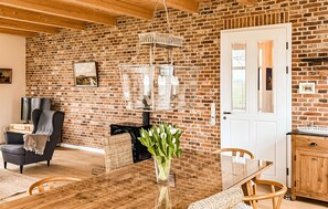 Ein Zimmer mit Backsteinwand, einem Esstisch mit Stühlen, einem Fernseher, einem Kamin und einer Tür.