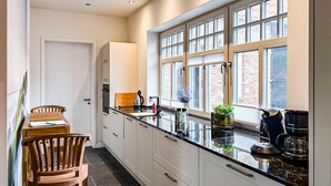 A narrow kitchen with white cabinets, a black countertop, and a window with a view of brick buildings. - Cozy home in Detern with WiFi (Detern)
