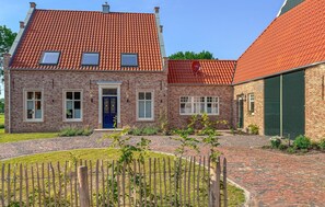 Ein zweistöckiges Backsteinhaus mit rotem Ziegeldach, einer blauen Tür und einem kleinen Garten mit Holzzaun.