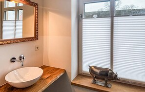 Ein Badezimmer mit einem weißen Waschbecken, einem Spiegel mit aufwendiger Rahmung und einem Fenster mit Jalousien.