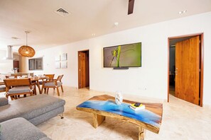 Ein modernes Wohnzimmer mit Couchtisch aus Holz, einem Essbereich mit Holztisch und Stühlen sowie einem an der Wand befestigten Fernseher.