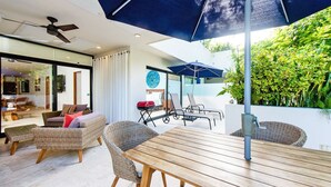 A modern outdoor patio with wicker furniture, a wooden table, and umbrellas providing shade. - Big Terrace Luxury 2-bedroom condo in charming Playa del Carmen with AC (Playa del Carmen)