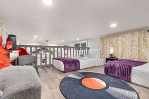 A modern hotel room with a balcony, a bed with a purple throw, a round rug with a vinyl record design, and a staircase leading to an upper level. - Firefly Music Row | 1BR + Loft | Fire Pit (Fredericksburg)