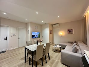 A modern living room with a dining area, a sofa set, a TV mounted on the wall, and a clock.