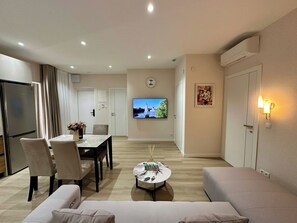 A modern living room with a dining area, a flat-screen TV mounted on the wall, and a sofa.