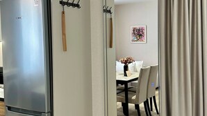 Ett modernt kök med ett kylskåp i rostfritt stål från Bosch, en trädörr och en matplats som syns genom en spegel.