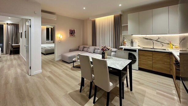 Ett modernt hotellrum med en matplats, en soffa, ett litet bord med stolar, ett köksutrymme och ett badrum.