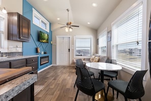 A modern kitchen with dark wood cabinets, a blue accent wall, and a dining area with a round table and black chairs. - Hill Country Hideaway| Pet Friendly (Fredericksburg)