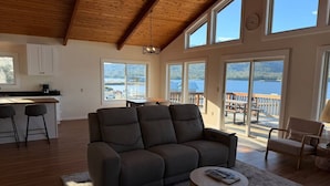 A spacious living area with a sofa, a coffee table, and a view of a lake through large windows. - Waterfront Fishing Lodge | 2BR | Dockside Charters (Ketchikan)