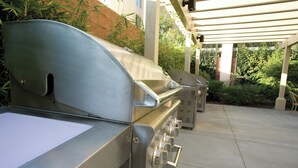 A commercial kitchen with stainless steel appliances, including a grill and ovens, under a covered outdoor area with greenery in the background. - 2-bedroom hotel suites in terrific Anaheim with fitness room and AC (Anaheim)
