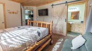 A wooden bedroom with a bed, a TV, a sliding door, and a small bathroom. - Yellowstone Park in 30 mins with Sauna & Hot Tub (Island Park)