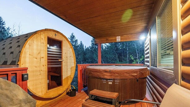 A wooden cabin with a hot tub, a deck, and a large log structure. - Yellowstone Park in 30 mins with Sauna & Hot Tub (Island Park)