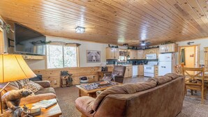 A cozy cabin interior with a wooden ceiling, a living room with a brown sofa and a coffee table, a kitchen area with wooden cabinets and appliances, and a dining area with a table and chairs. - Yellowstone Park in 30 mins with Sauna & Hot Tub (Island Park)