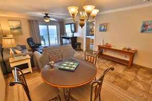 A living room with a round table, chairs, a sofa, a TV, and a balcony with a view. - Moonspinner 716 Panama city Beach Beach Front (Panama City)