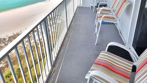 Un balcón con vista a la playa y al océano, sillas blancas y una puerta.